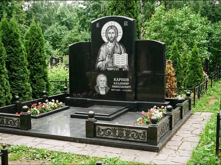 Памятник с гравировкой иконы: широкая панорамная стела с золочёным нимбом — гравировка образа Матроны Московской, цветник с белыми хризантемами, работа «Мельникова» в Набережных Челнах