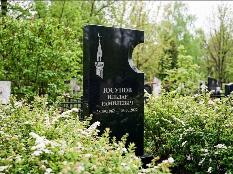 Мусульманский памятник с гравировкой мечети: стела с боковым вырезом в форме полумесяца — гравировка минарета с полумесяцем, низкие кусты спиреи в цвету, работа «Юсупов» в Набережных Челнах